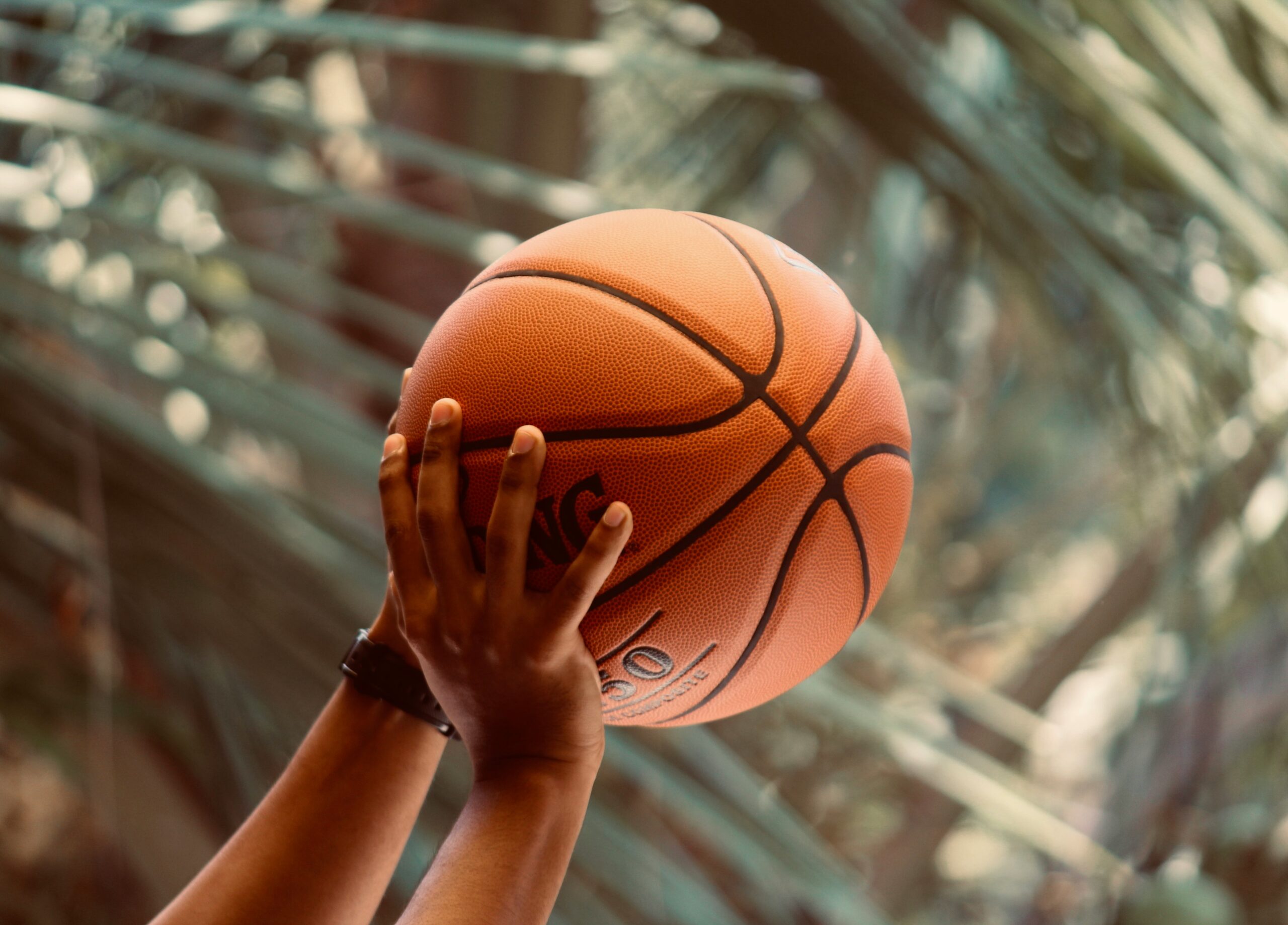 Close up photograph of basketball held by two hands in an upward motion with the stadium roof visible in the distance